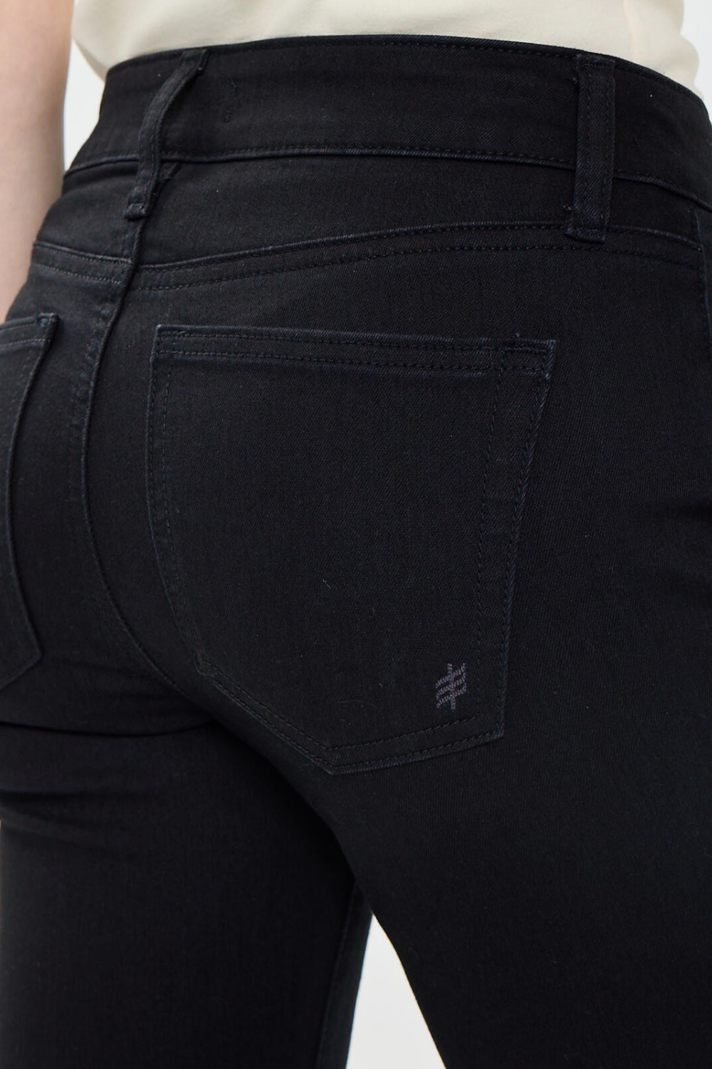 Close up of a woman, from behind, wearing black jeans with a sleeveless white top against a light backdrop.