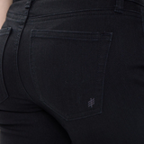 Close up of a woman, from behind, wearing black jeans with a sleeveless white top against a light backdrop.