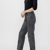 A woman modeling a pair of cropped black and gray leopard-print pants, paired with a black long-sleeve scoop-neck top and black mule heels, against a light gray studio background.