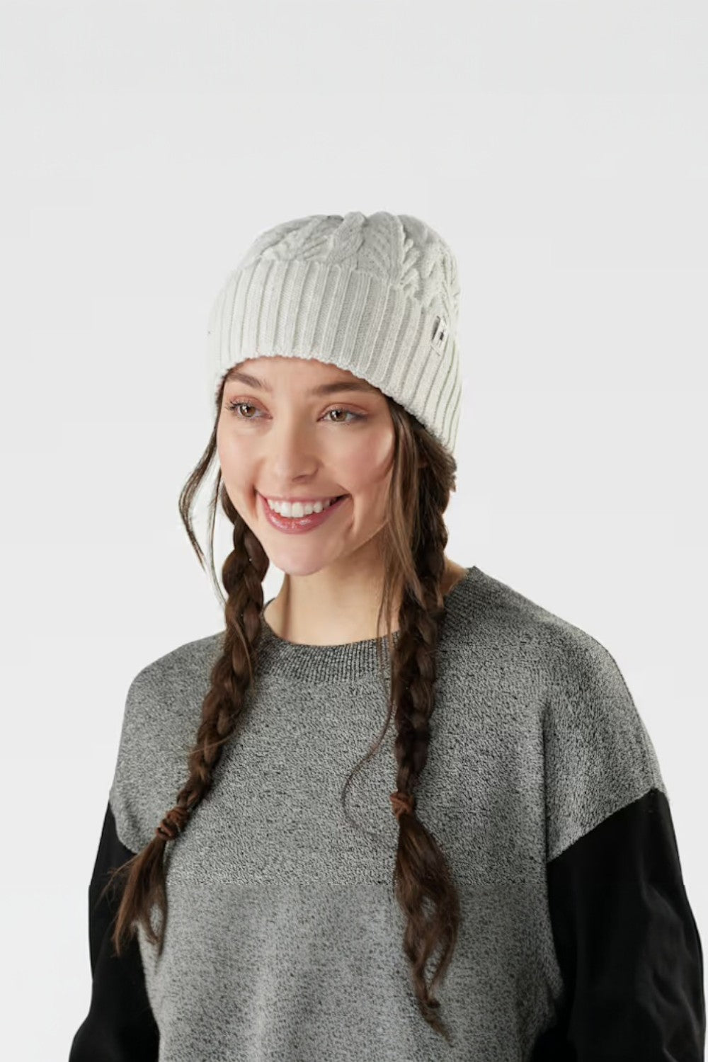 Woman wearing a natural knit beanie and sweater with braided hair on a white background