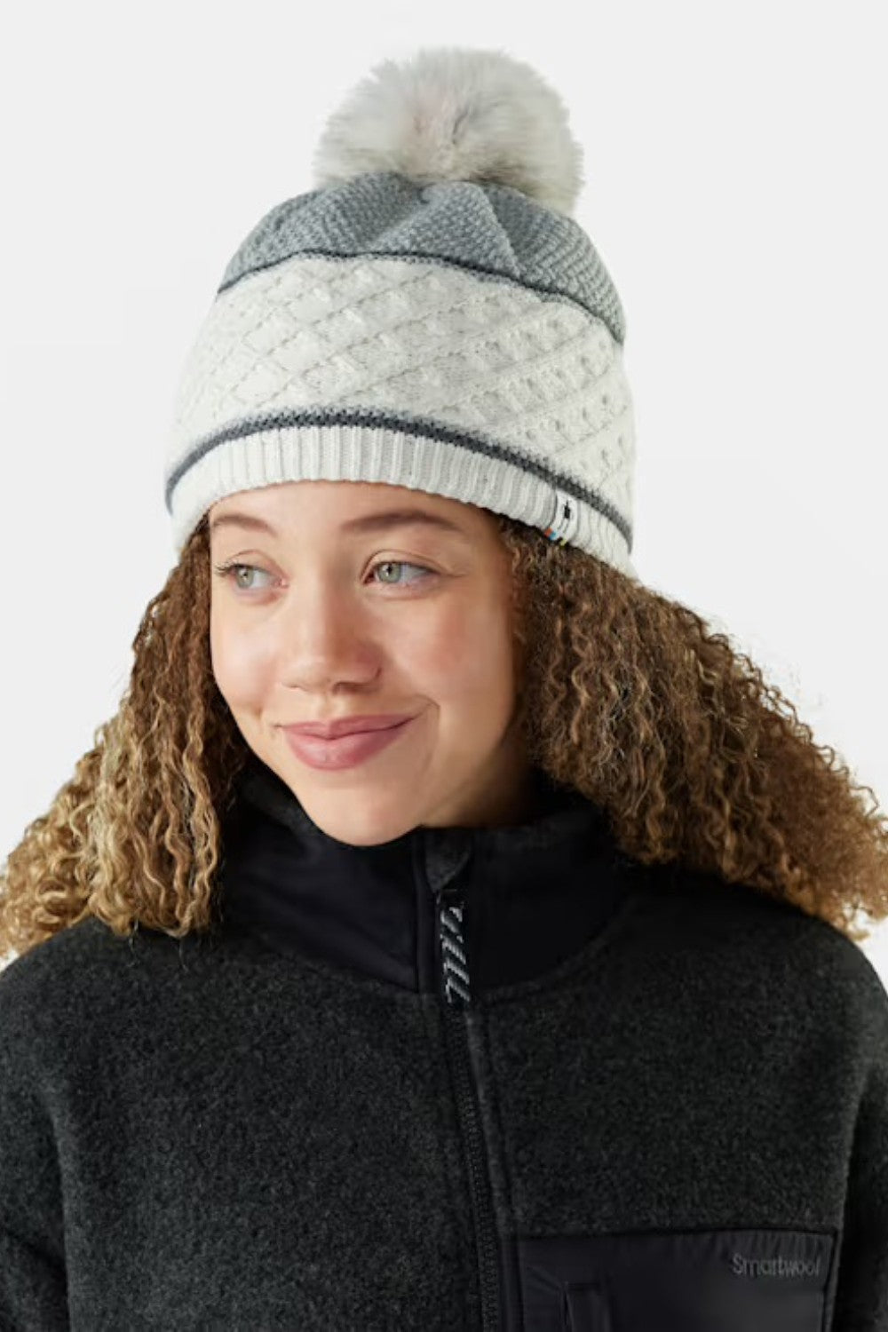 Person wearing a gray and white beanie with a pom-pom on a white background