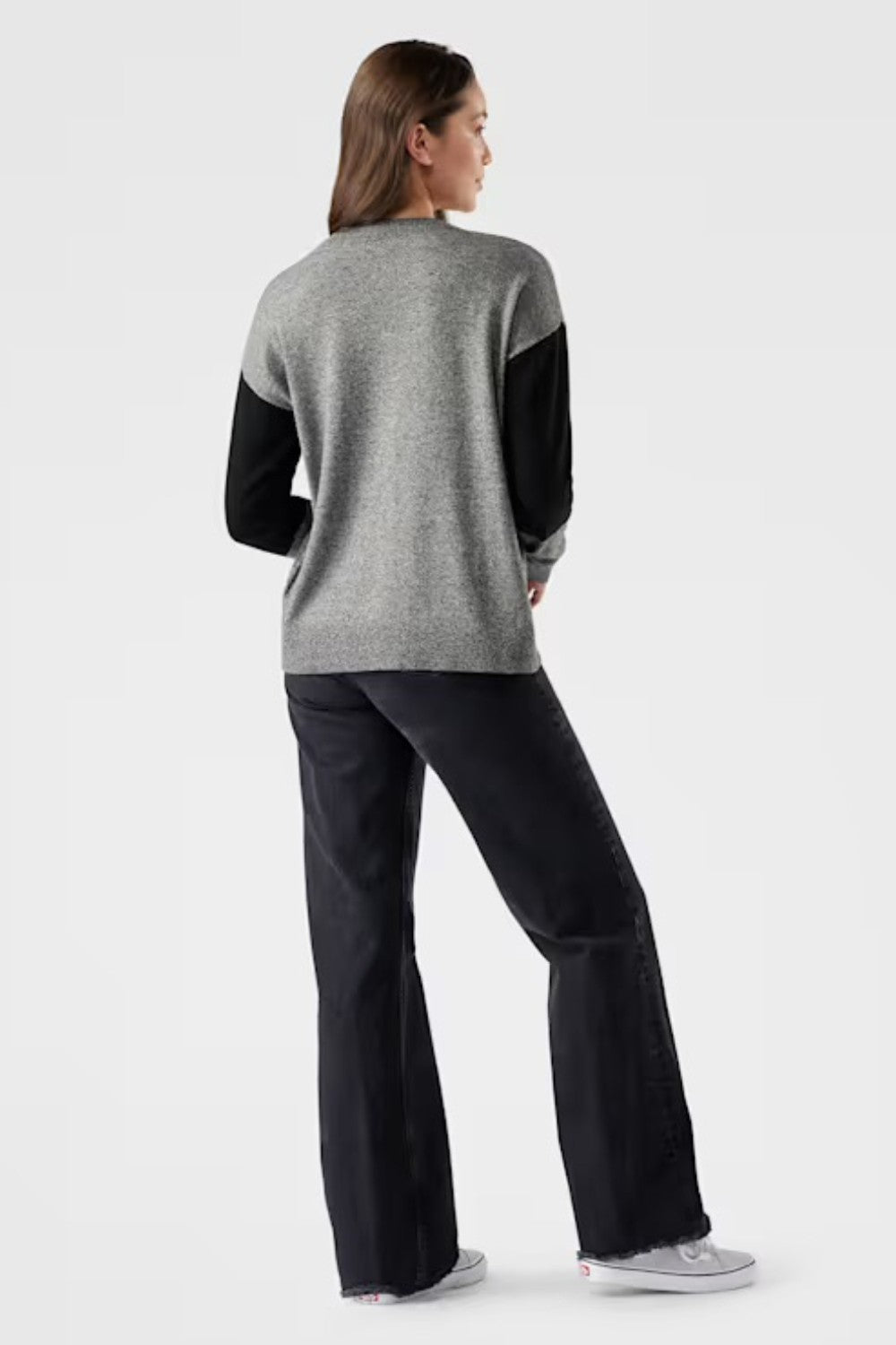 Woman wearing a gray sweater with black sleeves and black pants on a white background