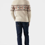 Man wearing a cream sweater with a pattern and dark jeans on a white background