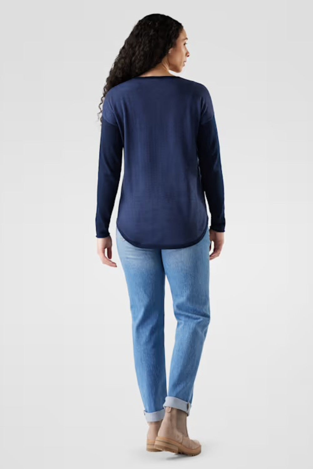 Woman wearing a navy long-sleeve top and light blue jeans on a white background