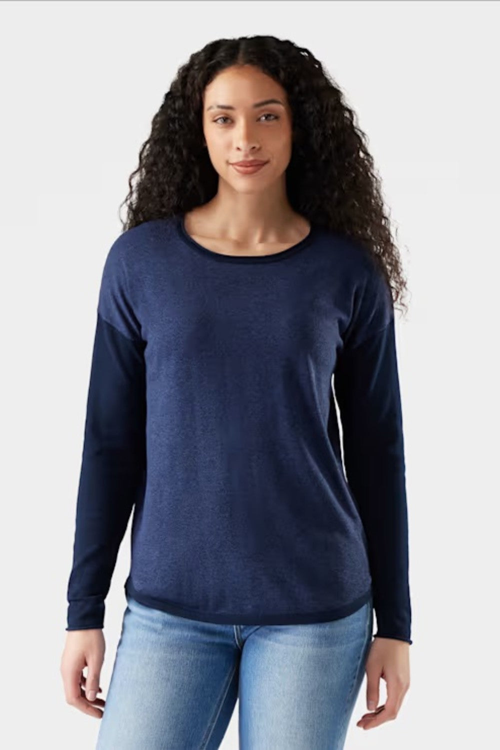 Woman wearing a navy long-sleeve shirt and light blue jeans on a white background