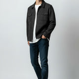 A man modeling a dark charcoal gray textured overshirt jacket over a white t-shirt, paired with dark blue jeans and white sneakers, standing against a light gray studio background.