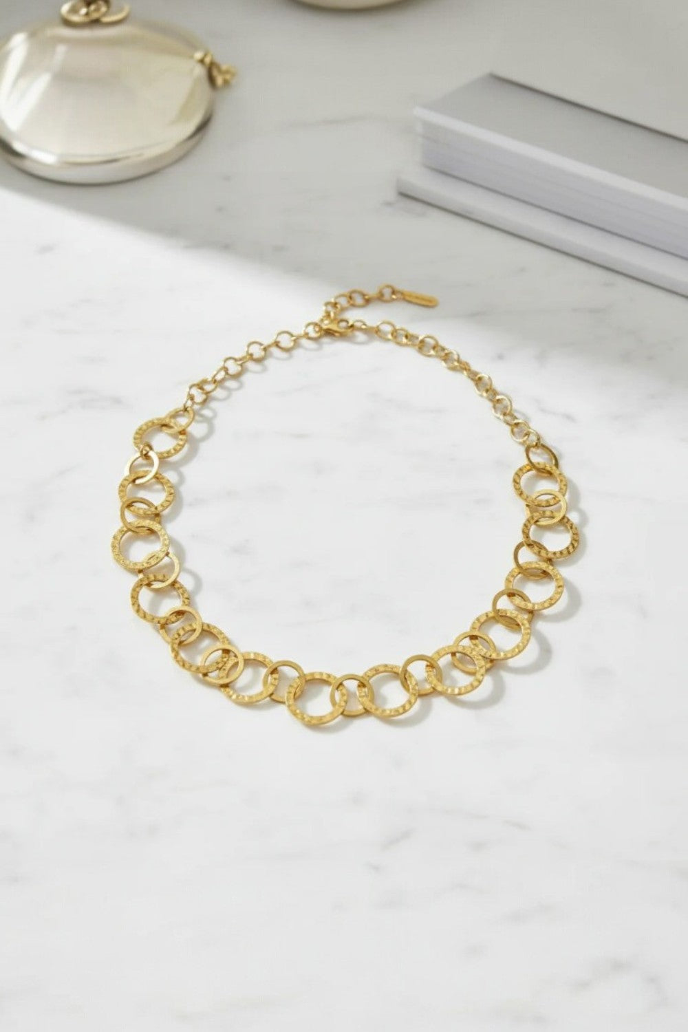 Gold necklace with circles looped together on marble surface