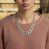 Woman wearing a pink sweater and silver chain necklace with a blurred outdoor background