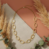 Gold chain necklace on a neutral fabric background with pampas grass and eucalyptus leaves.