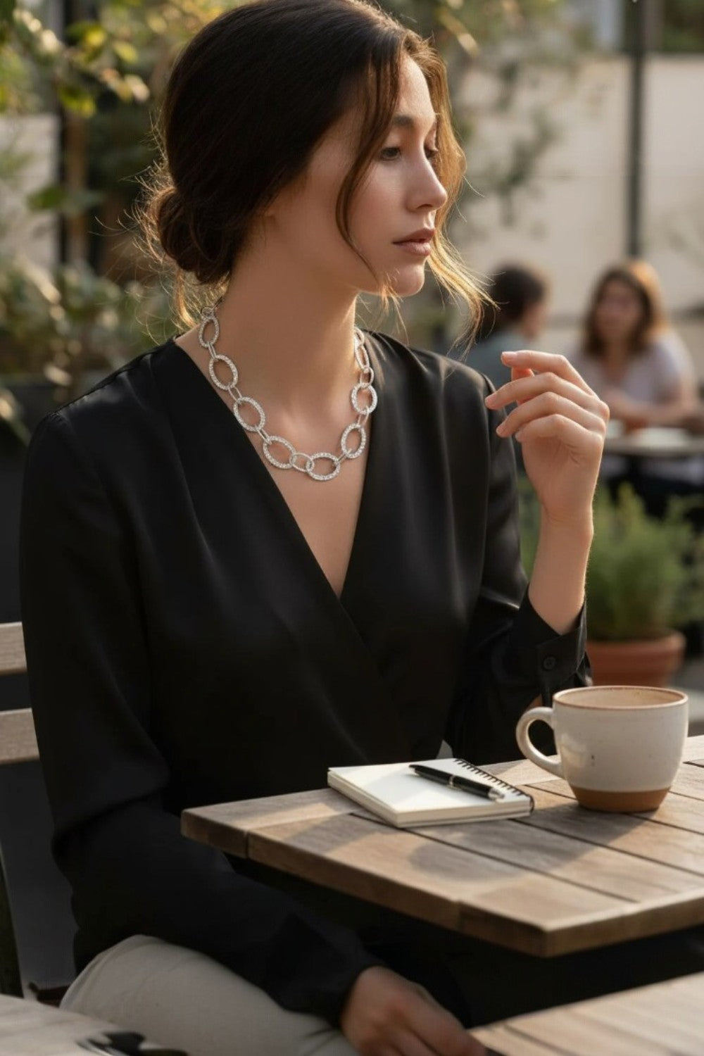 Woman sitting at an outdoor cafe table with a cup of coffee and notebook.