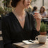 Woman sitting at an outdoor cafe table with a cup of coffee and notebook.