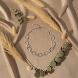 Silver chain necklace on a beige fabric background with dried grass and green leaves.