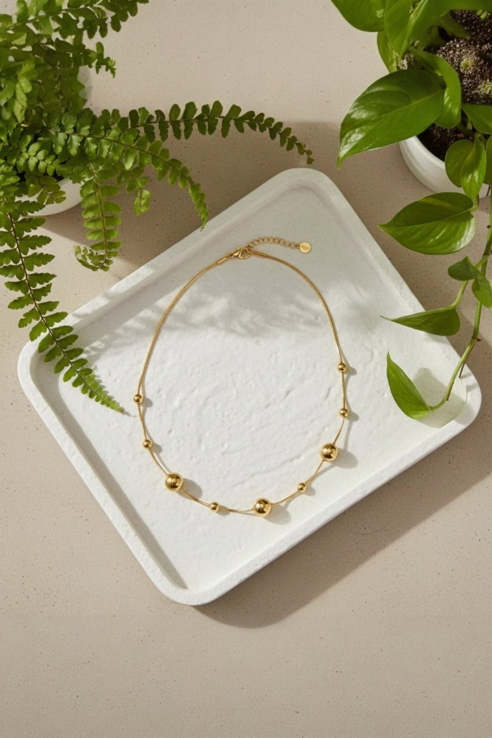 Gold necklace on a white textured tray with green leaves in the background