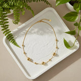 Gold necklace on a white textured tray with green leaves in the background
