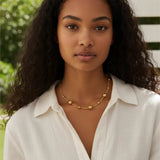 Woman wearing a gold necklace outdoors with greenery in the background