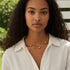 Woman wearing a gold necklace outdoors with greenery in the background