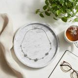 Necklace on a marble plate with a plant, tea cup, and glasses on a light surface