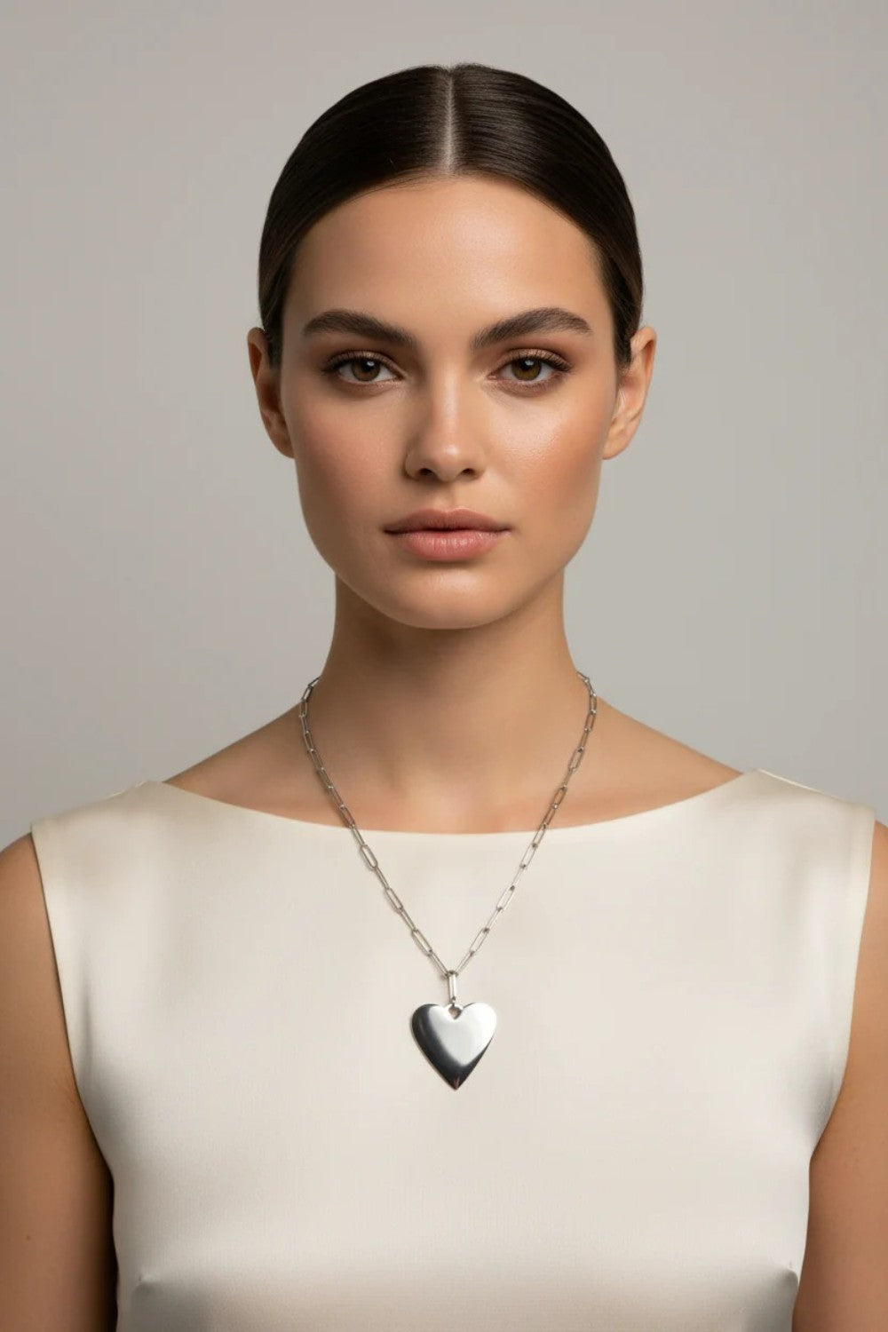 Woman wearing a silver heart-shaped necklace against a neutral background