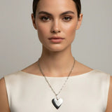 Woman wearing a silver heart-shaped necklace against a neutral background