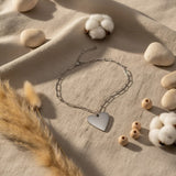 Heart-shaped pendant necklace on a textured surface with cotton and stones
