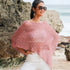 Woman wearing a pink knitted poncho and sunglasses on a beach.
