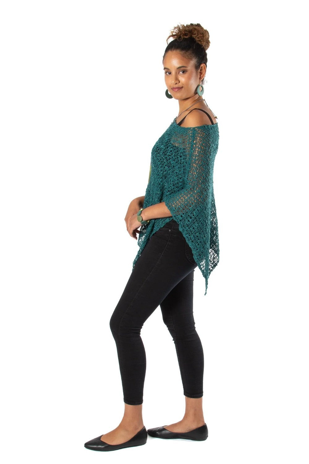 Woman wearing a green knitted poncho and black leggings on a white background