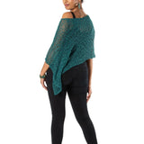 Woman wearing a green knitted poncho and black pants on a white background