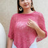 Woman wearing a pink knitted shawl against a beige wall.