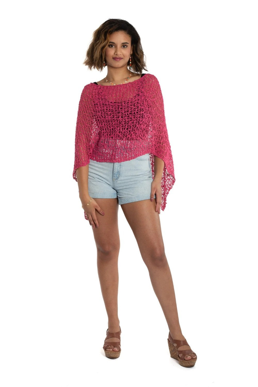 Woman wearing a pink crochet top and light blue shorts on a white background