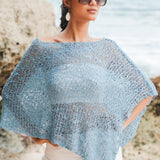 Woman wearing a light blue crochet poncho with white pants in an outdoor setting