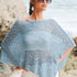 Woman wearing a light blue crochet poncho with white pants in an outdoor setting
