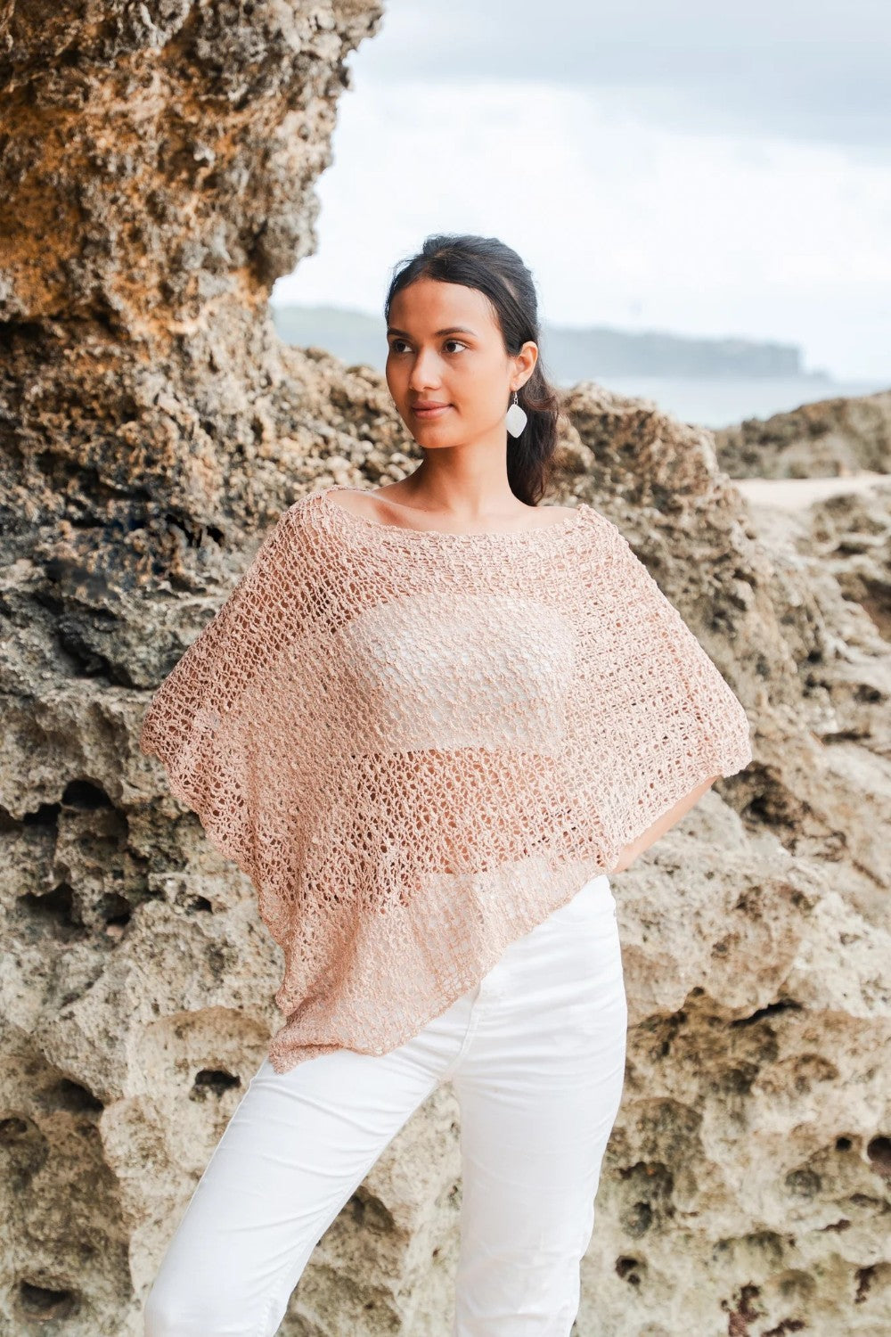Woman wearing a light crochet poncho with white jeans in an outdoor setting