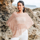 Woman wearing a light crochet poncho with white jeans in an outdoor setting