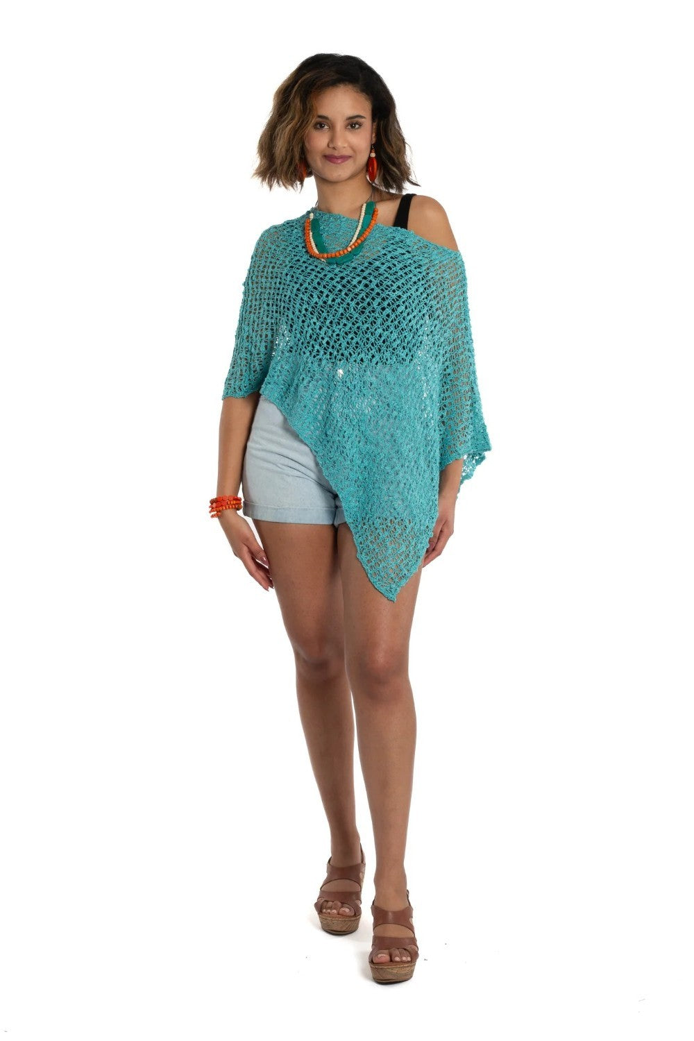 Woman wearing a teal knitted poncho over a white top and shorts on a white background