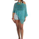 Woman wearing a teal knitted poncho over a white top and shorts on a white background