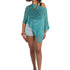 Woman wearing a teal knitted poncho over a white top and shorts on a white background