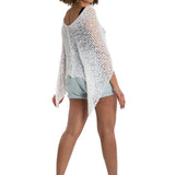 Woman wearing a light-colored crochet poncho over a white background