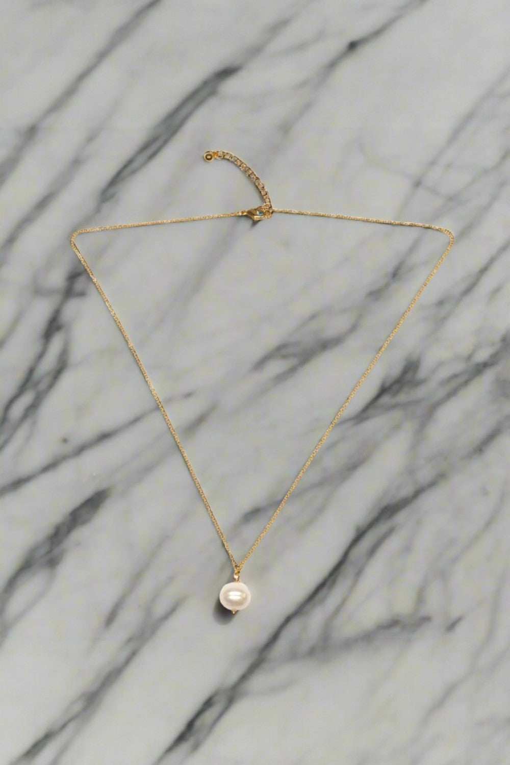 Gold necklace with a pearl pendant on a marble background