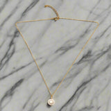 Gold necklace with a pearl pendant on a marble background