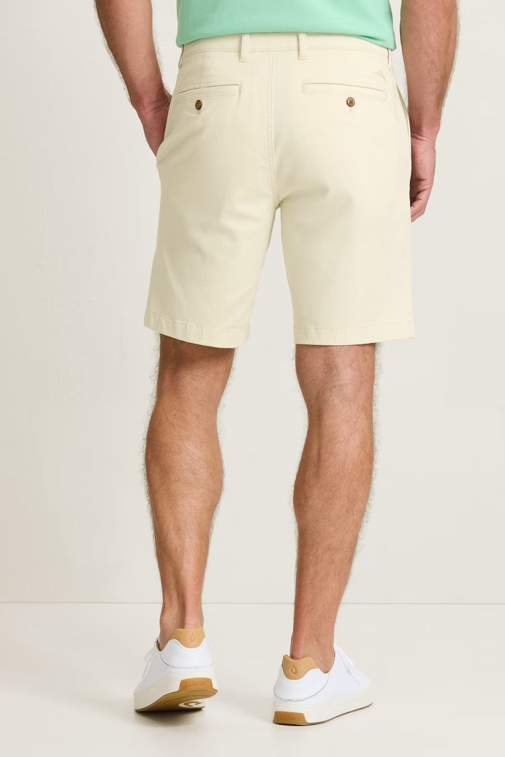 Person wearing beige shorts and white sneakers on a plain background