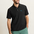Man wearing a black polo shirt with a small logo and green shorts on a beige background