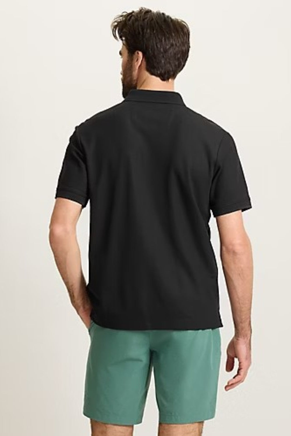 Man wearing a black polo shirt and green shorts on a beige background