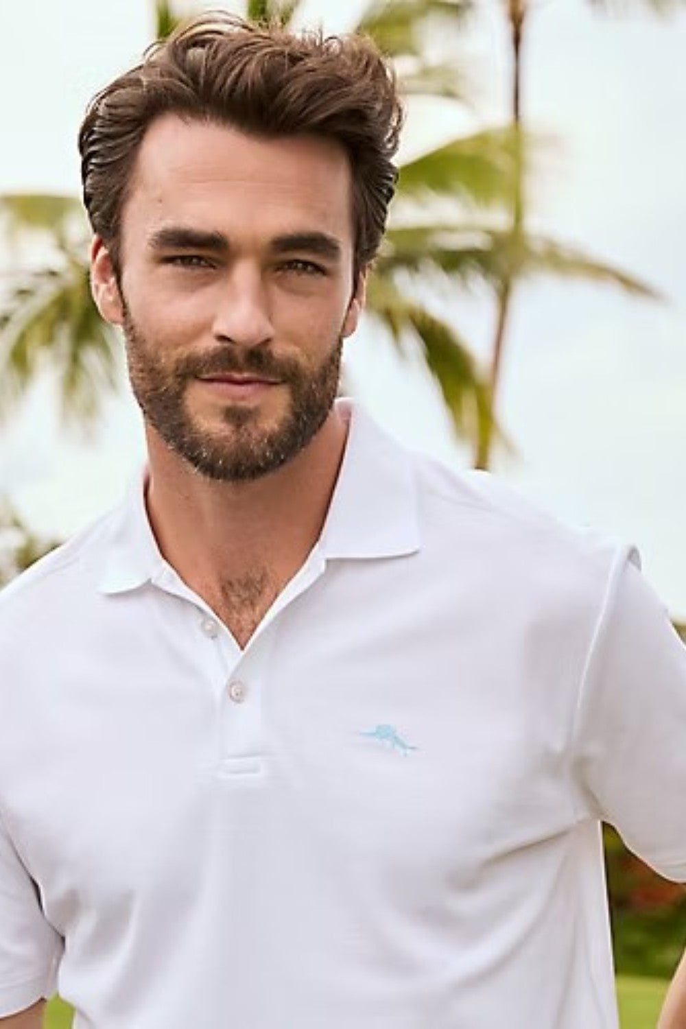 Man wearing a white polo shirt with a logo outdoors