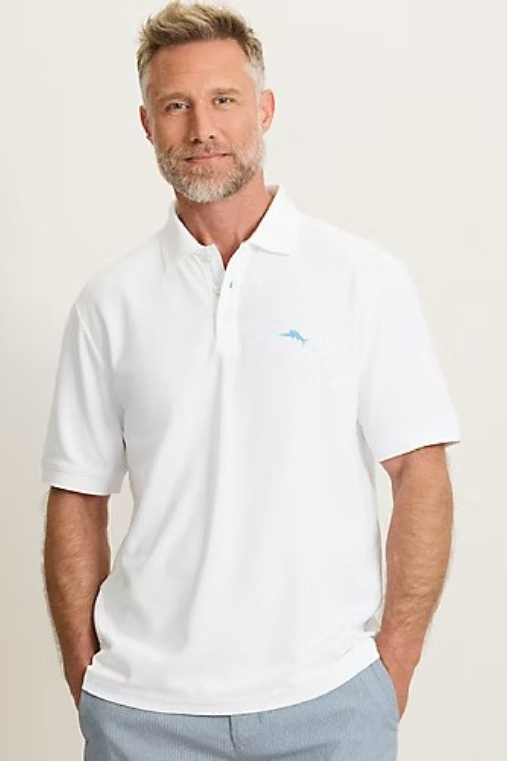 Man wearing a white polo shirt with a small logo on a plain background