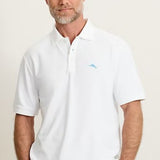 Man wearing a white polo shirt with a small logo on a plain background