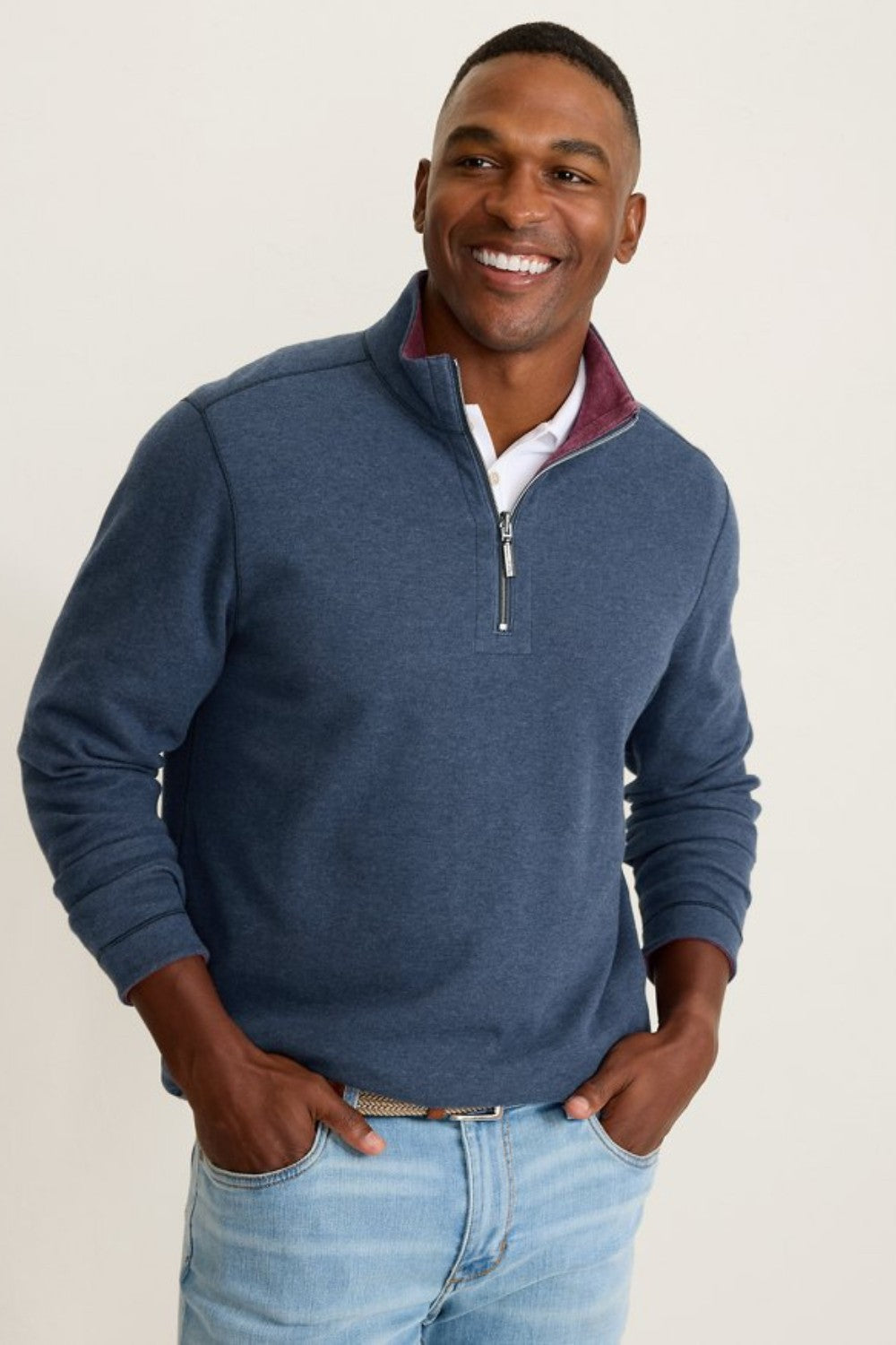 Man wearing a blue quarter-zip sweater with a white shirt underneath on a beige background