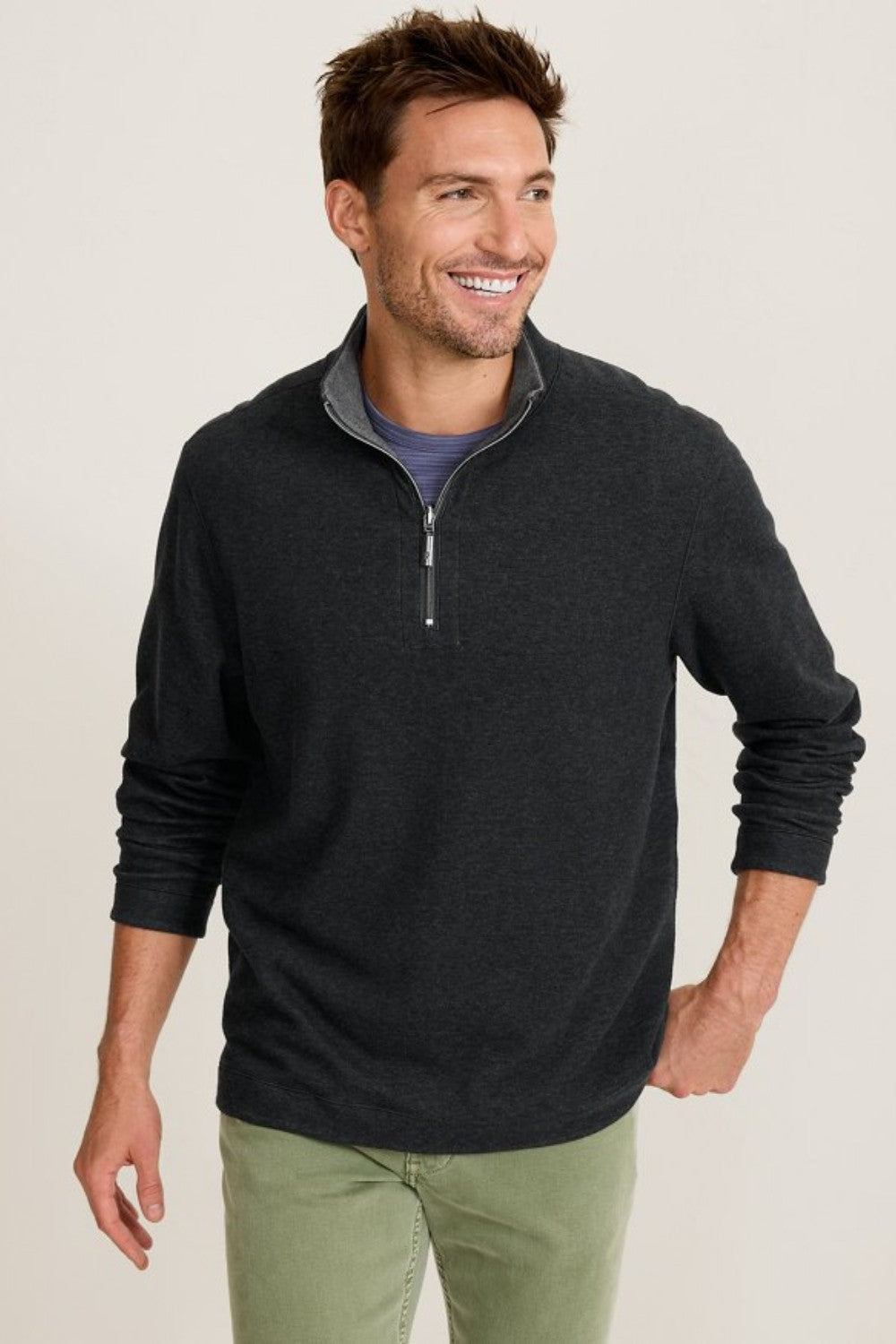 Man wearing a black half-zip sweater and green pants on a beige background