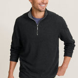 Man wearing a black half-zip sweater and green pants on a beige background