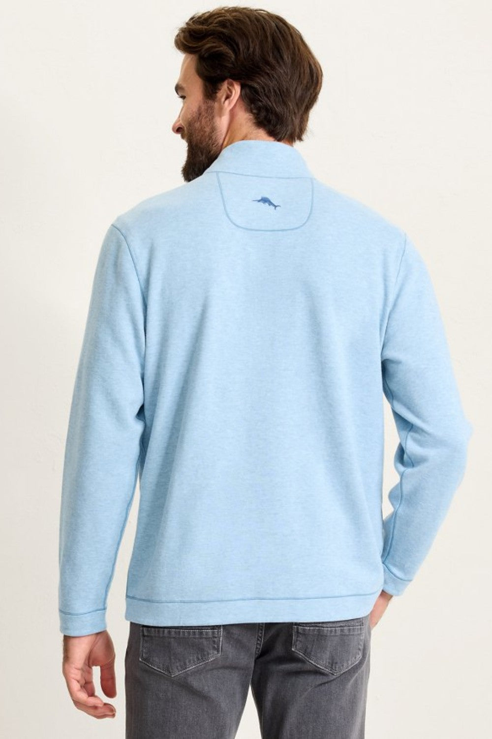 Man wearing a light blue pullover with a logo on the back against a plain background
