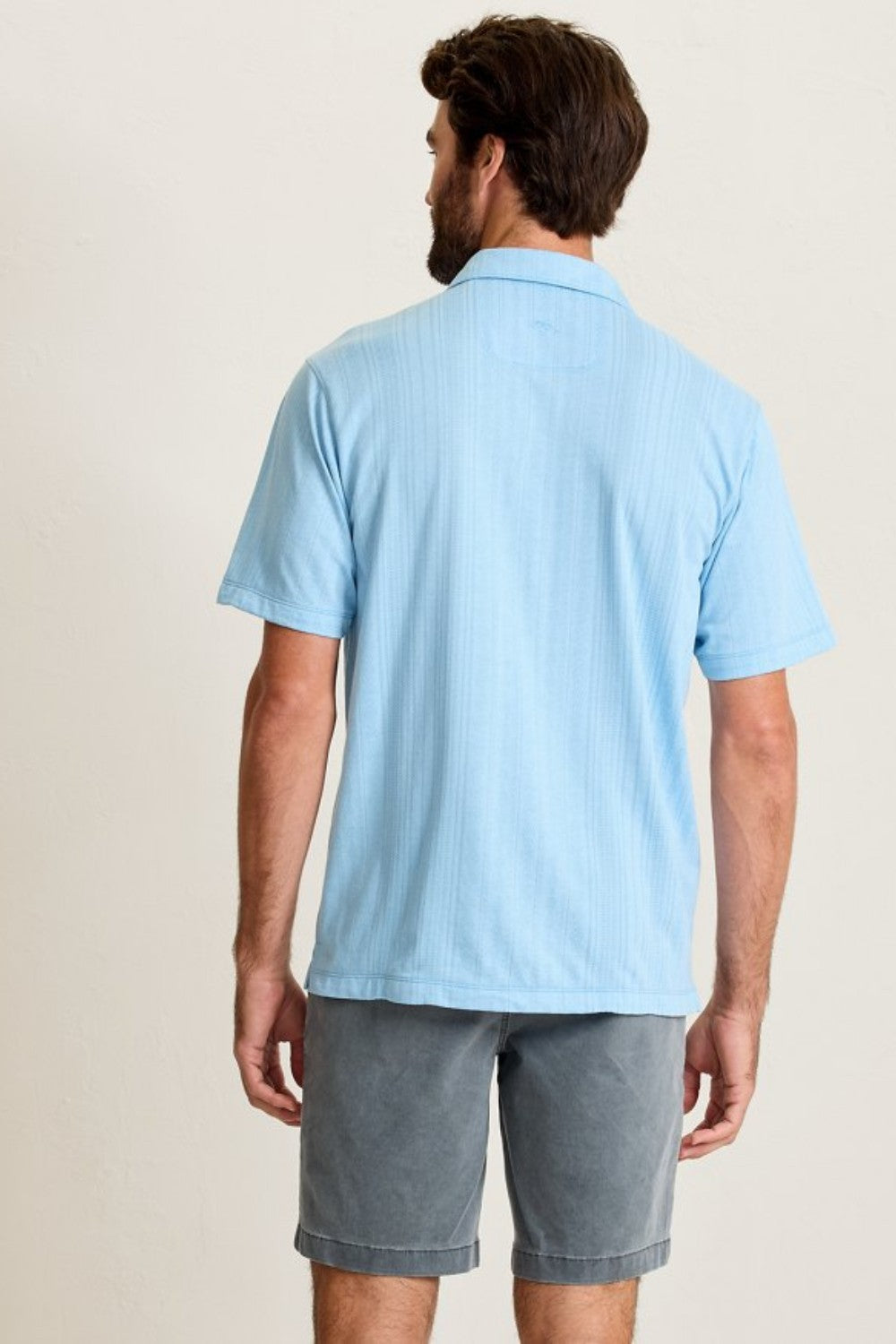 Man wearing a light blue polo shirt and gray shorts on a beige background